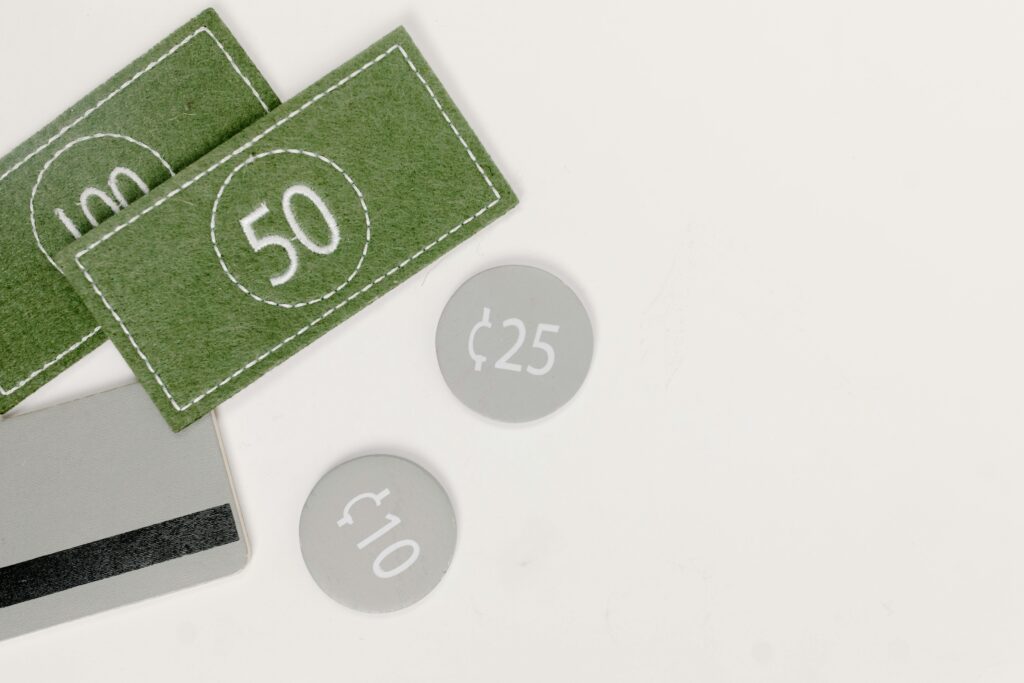 Felt play money including green bills labeled 50 and 100, round gray coins labeled ¢25 and ¢10, and a toy credit card on a white background.